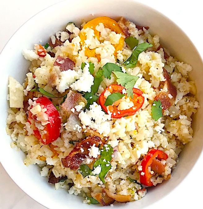 meican cauliflower rice in a bowl with cilantro, red bell pepper, cotija cheese and bacon