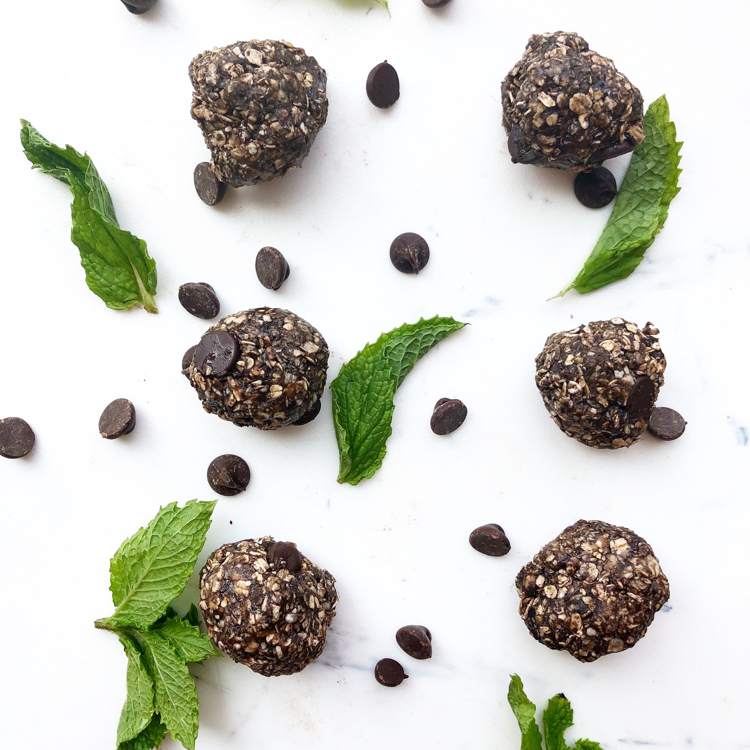 mint chocolate protein balls on a white background with fresh mint and chocolate chips scattered